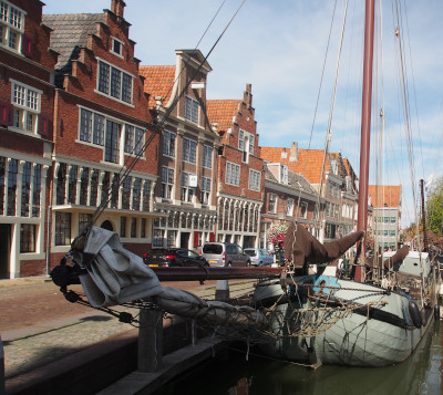 Two sailboats are parked in front of a row of quaint old Dutch buildings.