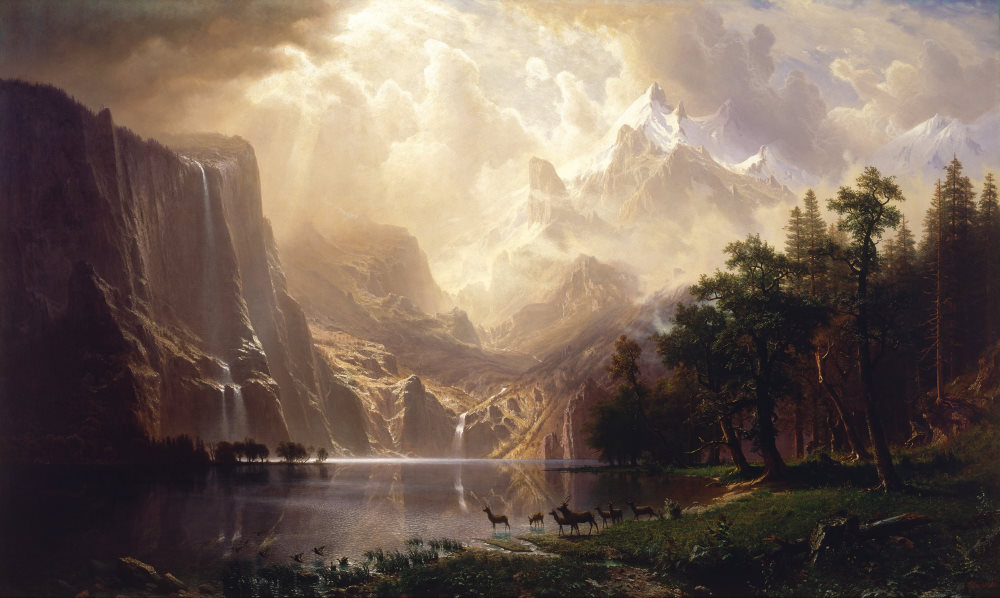 In the background, mountains soar through the sky; in the foreground, deer rest by a lake