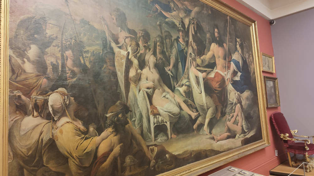 In a gallery hangs a large landscape painting depicting the Gods and Goddesses of the classical world