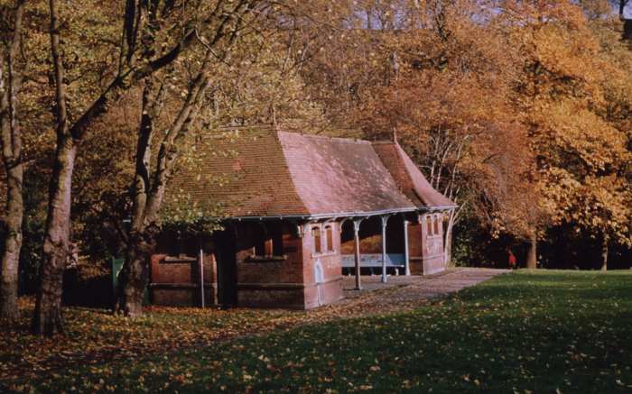 A small covered shelter in a park surrounded by auburn-leaved trees.