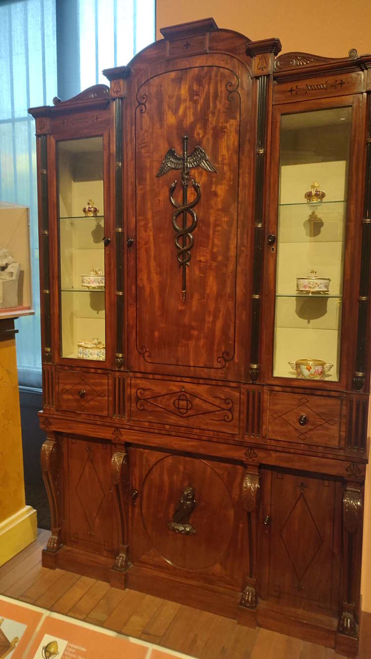 A dark wooden cabinet whose middle is adorned with a beautiful embossed caduceus