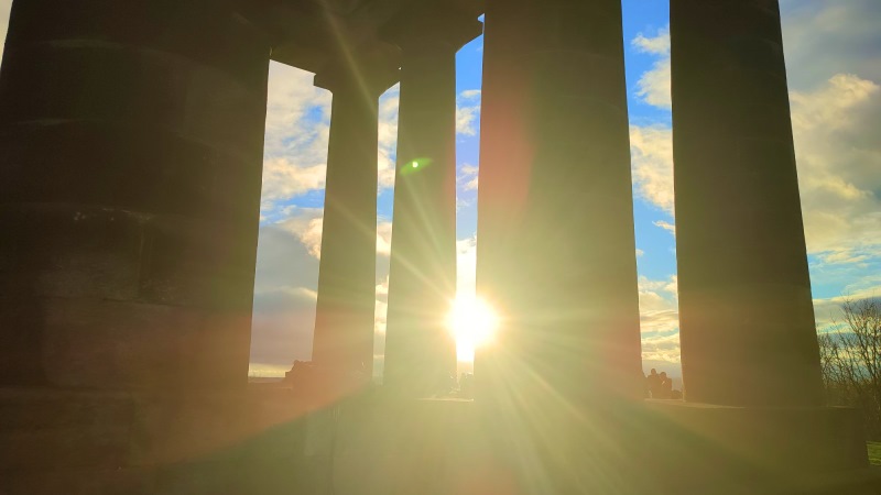 The sun shines through the monument's columns.