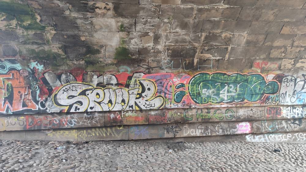 Graffiti covers the walls of an archway underpass, its floor  tiled with loose cobbles