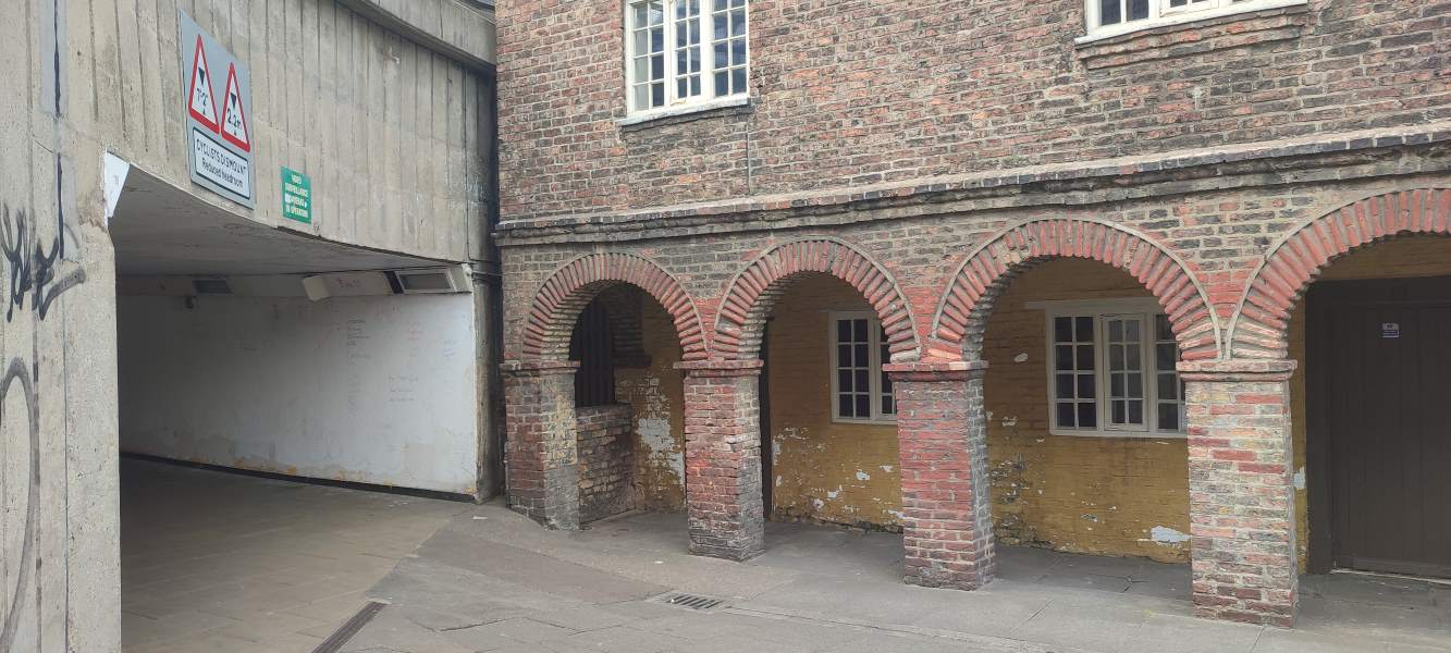 A decaying building’s brick-arched frontage contrasts with a concrete underpass.