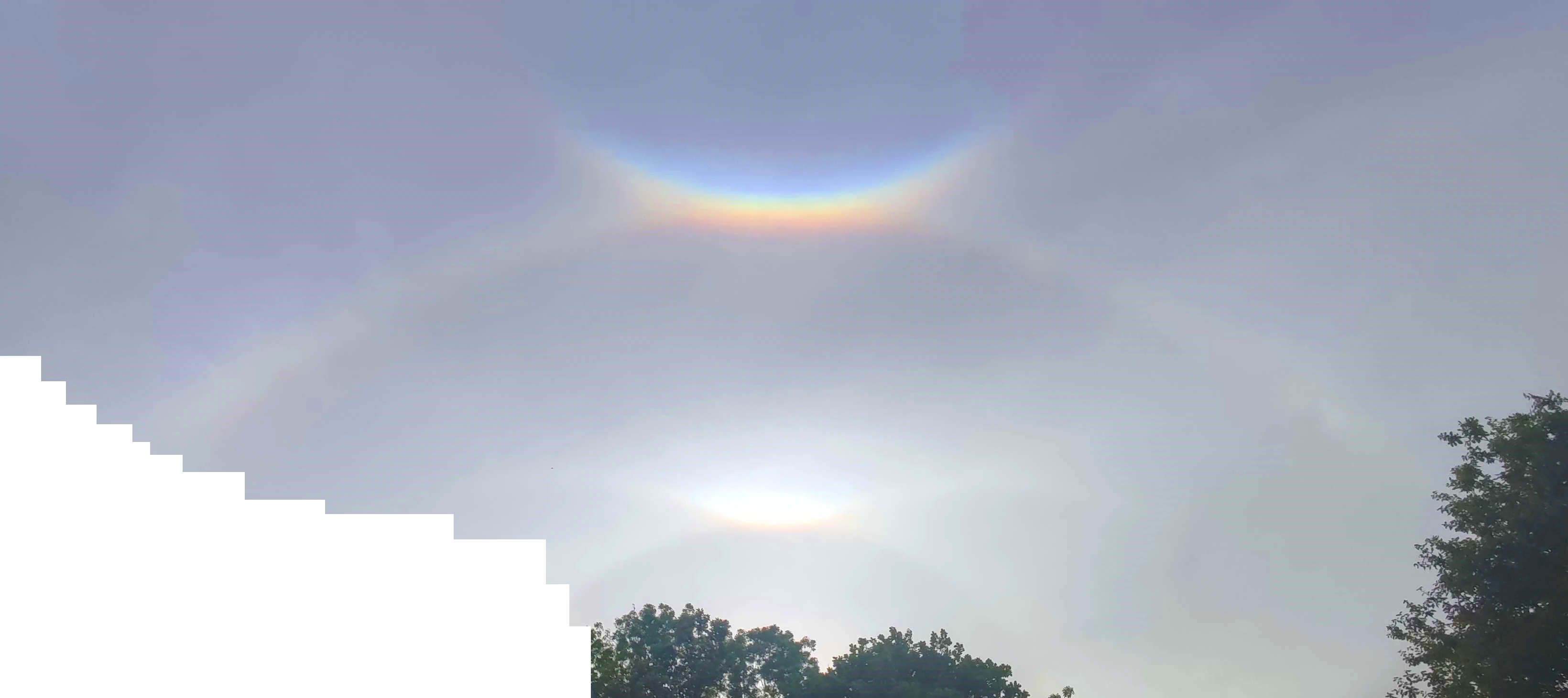 Two iridescent arcs intersect in the sky, a smaller version of the same phenomenon playing out below
