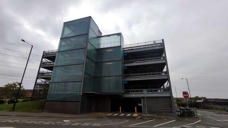 A modern car park with frosted glass panels juts into the cloudy sky.