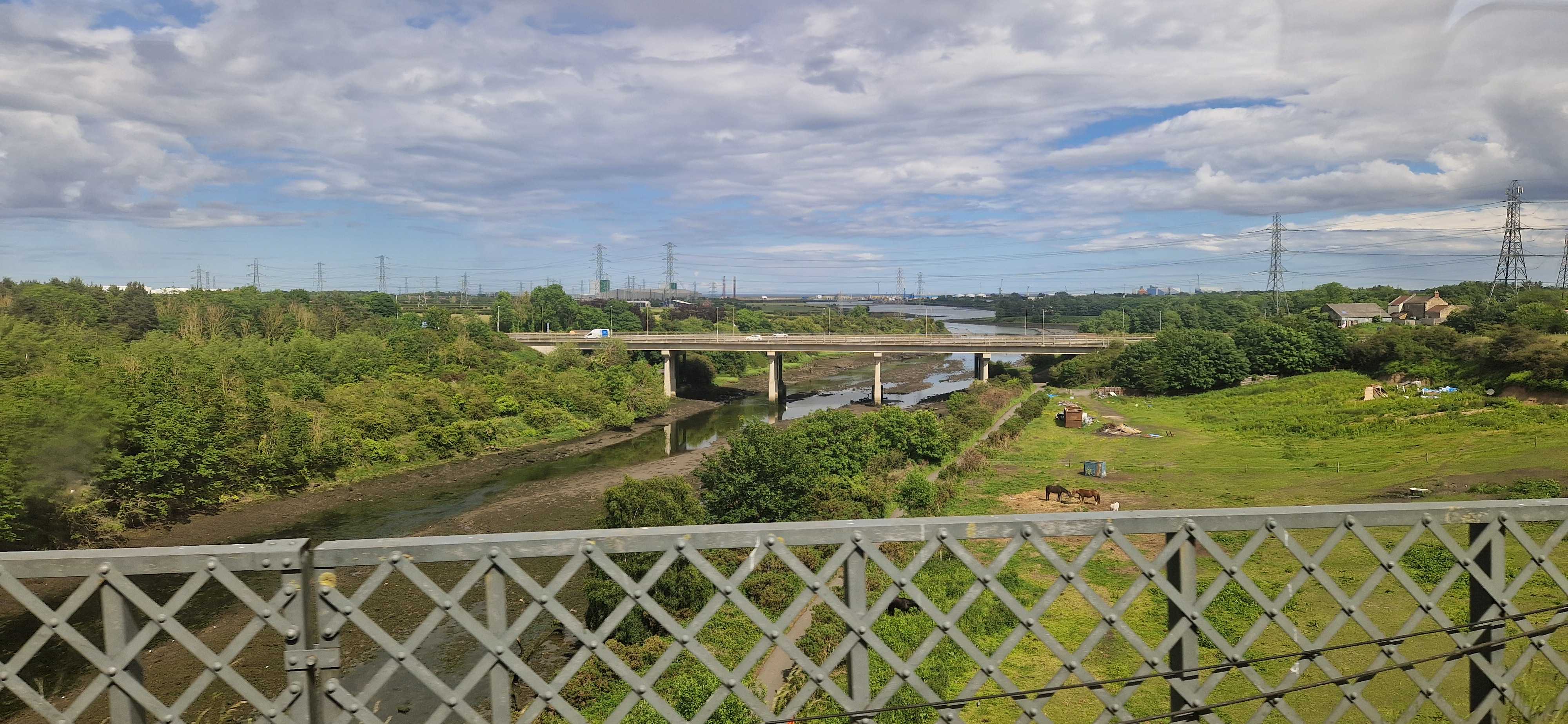 Looking over at a road viaduct over the River Blyth and out to sea, in a low-lying landscape dominated by trees and pylons